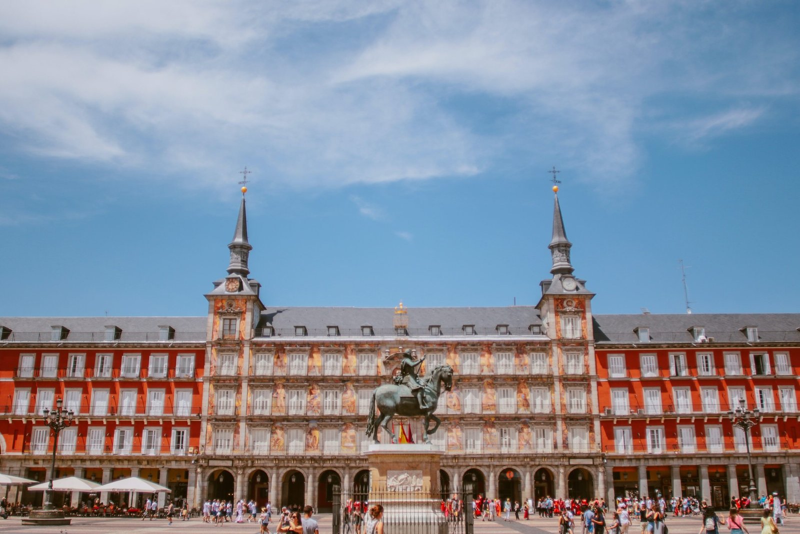 "La imagen muestra la céntrica y emblemática plaza del Sol de Madrid, con su característica estatua ecuestre de Carlos III en el centro, y edificios históricos como la Casa de Correos y el edificio que alberga al Ministerio de Gobernación rodeando la plaza. Esta plaza madrileña es un punto de encuentro tradicional y un icono de la capital española, por lo que ilustra perfectamente el ambiente histórico y cultural en el que se realizó el acto de la jura ante notario, transportando al lector a la enérgica vida de Madrid."